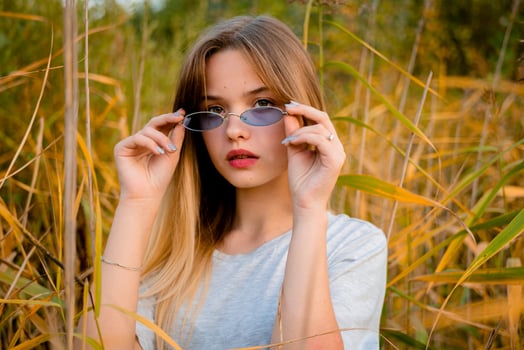 Beautiful young girl wearing blank gray t-shirt and black jeans in blue glasses posing against high green and yellow grass in early warm autumn. Outdoor portrait of beautiful female model. photo