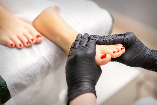 Foot massage with moisturizing and peeling cream by pedicurist hands wearing black gloves, close up. photo