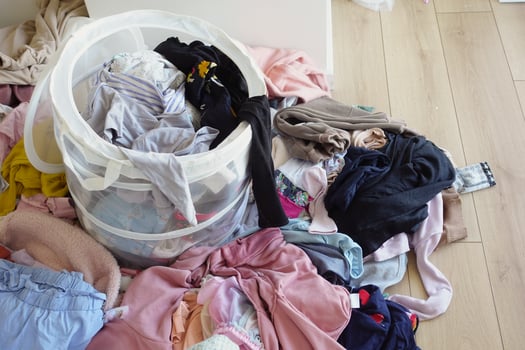 Clothes pile next to laundry basket filled with garments, on hardwood floor photo