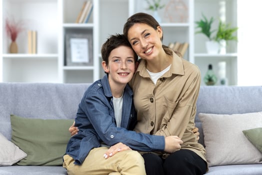 Portrait of family, mother and teenage son sitting on sofa at home and hugging, smiling at camera. photo