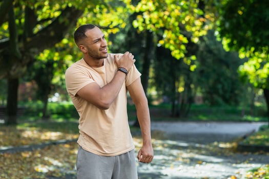 A man injured his shoulder during a fitness class, an African-American man injured himself while jogging in the park, stretches his arm and massages his sore muscles. photo