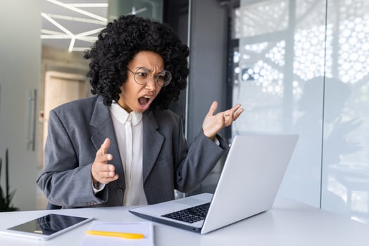 Shocked young african american business woman sadly looking at laptop screen on table and throwing hands in frustration. photo