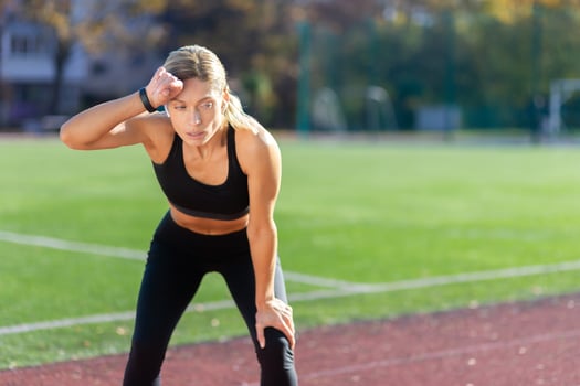 Tired sportswoman resting after jogging on a sunny day at the stadium, blonde in sportswear taking a breather. photo
