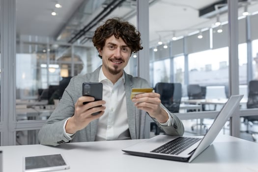 Curly-haired young businessman in a modern office multitasking with a laptop and smartphone, exemplifying focused corporate work. photo