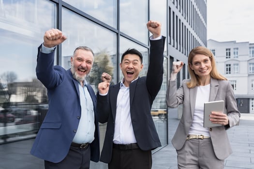 Successful diverse business team, three loving men and woman looking at camera and happy celebrating victory, team dreaming outside office building, business group in business suits photo
