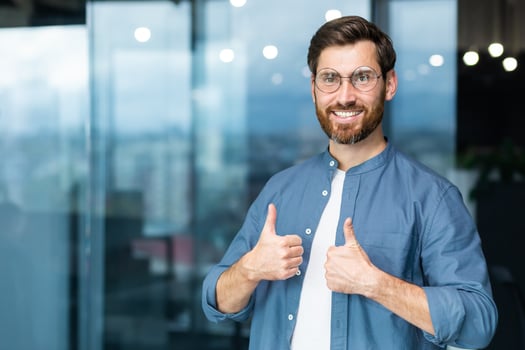 Portrait of businessman in casual shirt, man with beard and glasses smiling and looking at camera showing thumbs up affirmative, business owner working inside office. photo