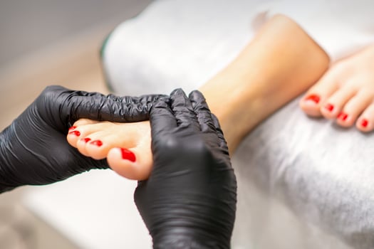 Foot massage with moisturizing and peeling cream by pedicurist hands wearing black gloves, close up. photo