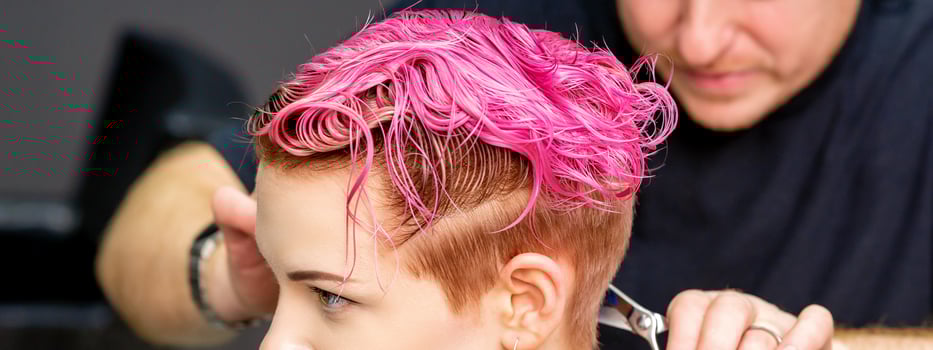 Woman having a new haircut. A male hairstylist is cutting dyed pink short hair with scissors in a hair salon. photo