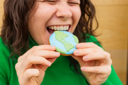 Earth Day concept. Woman bites into a cookie in the shape of the Earth. photo