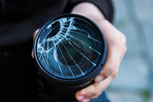 Hands of young photographer holding DSLR photo camera with broken lens filter glass after if fall down onto the floor. Close up. Destroyed cracked photo-filter. Macro. Top view. Selective focus.