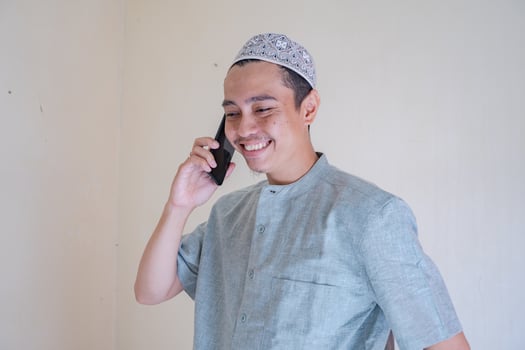 Moslem Asian man calling with smartphone with happy face when Ramadan celebration. The photo is suitable to use for Ramadhan poster and Muslim content media.
