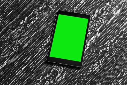 Black tablet with green screen on a wooden table mock up. Copy space chroma key display. photo
