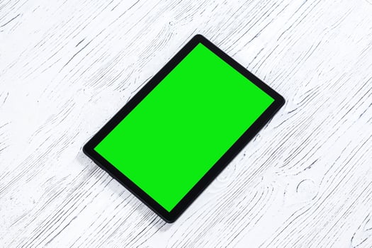 Black tablet with green screen on a wooden table mock up. Copy space chroma key display. photo