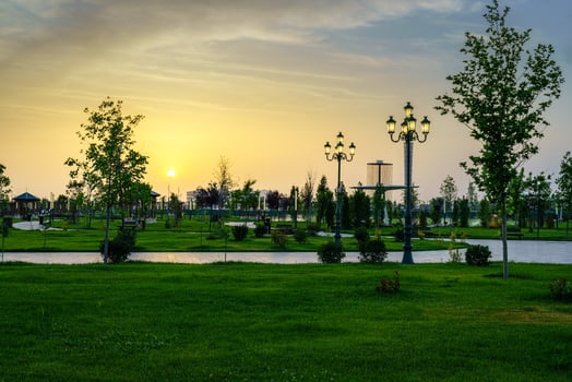 City park in early summer or spring with lanterns, young green lawn, trees and dramatic cloudy sky on a sunset or sunrise. photo