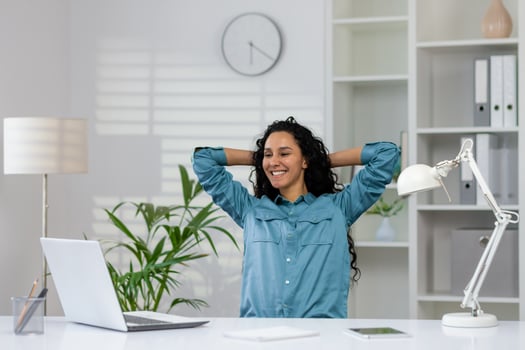 A professional rests with hands behind head, feeling relaxed in a bright, contemporary office space surrounded by work equipment. photo