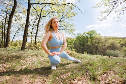 The girl extends her leg out to the side thereby stretching the leg muscles Beautiful blonde Caucasian woman in blue tight tracksuit. Blonde girl at an outdoor training session photo