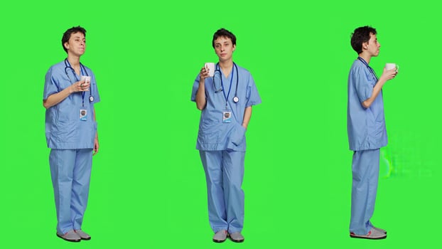 Medical assistant drinking cup of coffee before starting exam appointments in the morning, enjoying caffeine refreshment against greenscreen backdrop. Nurse drinks beverage. Camera A. photo