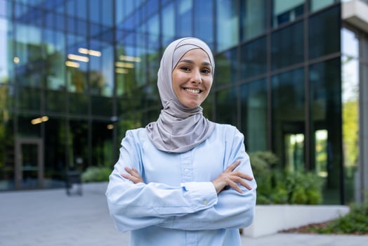 Professional young Muslim woman with a beaming smile, wearing a hijab, standing confidently outside an office. photo