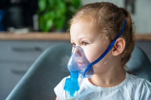 Cute little girl are sitting and holding a nebulizer mask leaning against the face, airway treatment concept. High quality photo