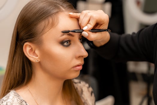 Make-up artist paints eyebrow pencil to beautiful brunette in be photo