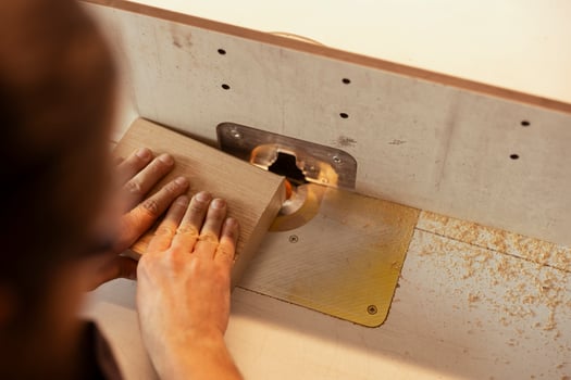 Carpenter in studio puts wood block through spindle moulder, creating smooth edges on wooden pieces. Cabinetmaker in carpentry shop using heavy machinery to craft strong seamless joints for furniture photo