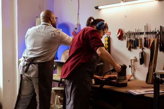 Master carpenter and apprentice using orbital sander on lumber, assembling furniture. Teamworking employees in assembly shop using angle grinder to create wooden decorations, refining wood objects photo