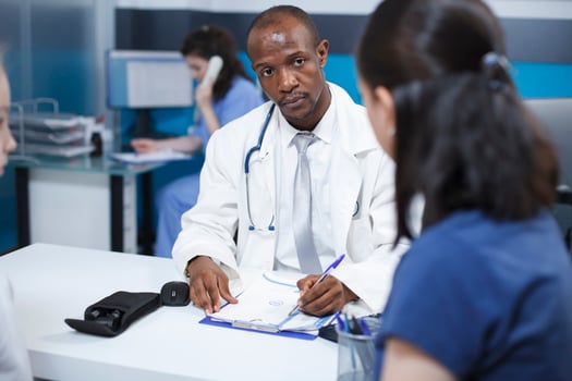 Black man wearing a lab coat, taking notes during a consultation with a female patient at the clinic. African American doctor explains the treatment plan, ensuring proper care. photo