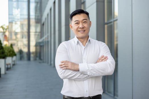 Portrait of a smiling and successful young businessman, office worker in a white shirt standing outside on the street, crossing his arms on his chest and looking confidently at the camera. photo