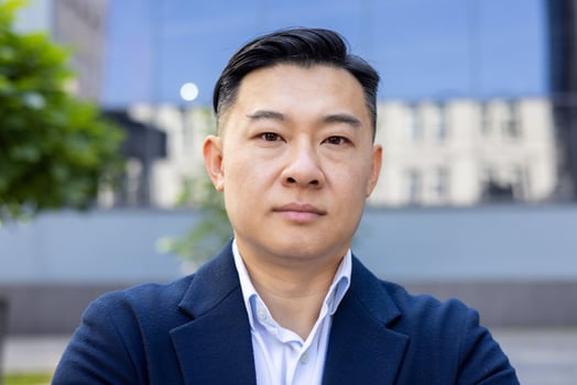 Confident Asian male executive in a stylish blue suit and white shirt, looking seriously at the camera outdoors. photo