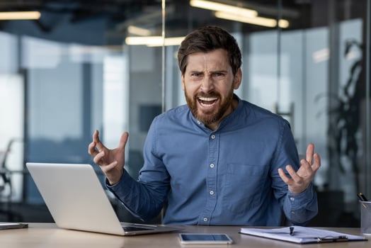 Portrait of an angry and irritated young businessman sitting at a desk in the office and shouting at the camera. photo