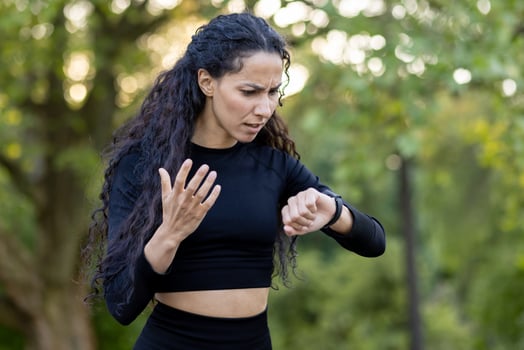 A confused Hispanic woman in workout attire checks her watch during an exercise session in a park, expressing uncertainty and slight frustration. photo