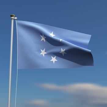 Micronesia Flag is waving in front of a blue sky with blurred clouds in the background photo