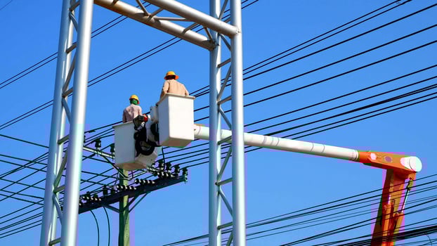 Two electricians on bucket boom truck are installing electrical system on power pole against blue clear sky background photo