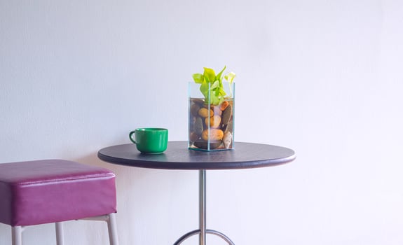 Green coffee mug and houseplant in glass vase on round table with leather chair near empty gray interior wall in minimal style photo