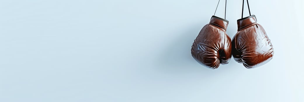 Brown leather boxing gloves hanging. Isolated on white backdrop. Banner with copy space. Minimalistic sports equipment concept. Design for poster, banner, sport-related advertising. Copy space. photo