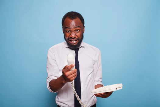 An enraged black businessman yells into the cord phone receiver, arguing with the person on the other end of the line. An anxious African American employee is on the phone with his manager. photo