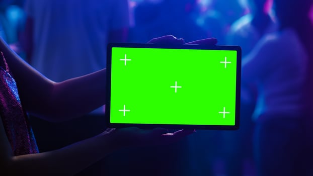Adult using tablet with green screen at club, holding gadget with blank mockup template on dance floor. Young woman showing isolated display with chroma key and copyspace at nightclub. photo
