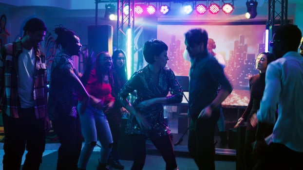 Men and women improvise dance battle at disco party, moving around dance floor with electronic music and stage lights. Young dancers having fun showing off funky moves. Handheld shot. photo