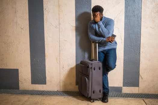 Worried man with suitcase and mobile phone leaning against a wall in passage of the railway station. Copy space on image for your advert or text. photo