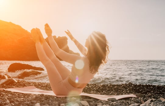 Woman sea yoga. Happy woman in white swimsuit and boho style braclets practicing outdoors on yoga mat by sea on sunset. Women yoga fitness routine. Healthy lifestyle, harmony and meditation photo
