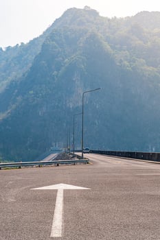 The scene of the road at the top of the dam, with the mountains in the background and a light pole. photo