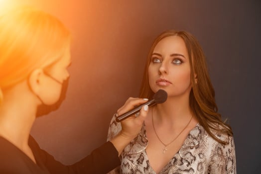 Makeup beauty salon. Makeup artist applies powder and blush. Beautiful female face. Makeup master's hand puts blush on cheeks of beauty model girl. Makeup in progress photo