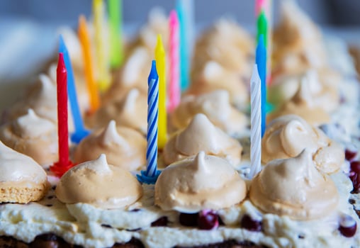 Birthday cake with white whipped cream, meringues and cranberries, decorated with multicolored lit candles. Happy Birthday concept. Tradition of making a wish blowing out candles. Selective focus. photo
