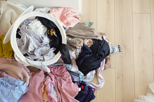 Clothes pile next to laundry basket filled with garments, on hardwood floor photo