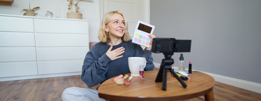 Portrait of beautiful lifestyle blogger, girl records a on her camera for social media, shows palette of eyeshadows, does a makeup tutorial for her followers, sits in her room photo