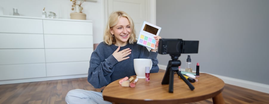 Portrait of beautiful smiling woman, recording in her room, has camera on coffee table, reviewing makeup, doing lifestyle vlog for social media account, records a tutorial photo