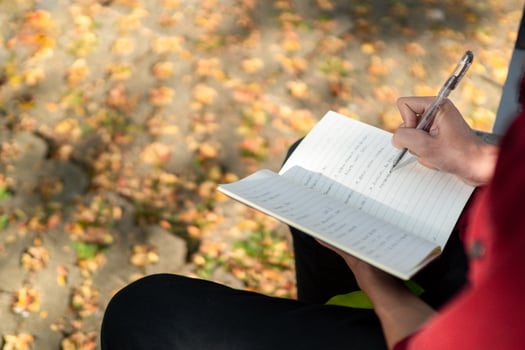 Asian college student studying on laptop at campus outdoor park. Man writing on a note book and working on laptop. Educational concept photo