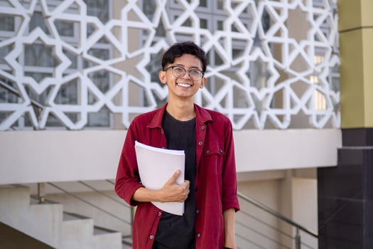 Asian college student smiling and looking. Portrait of a college student at campus. Asian male student standing holding a book looking at the camera. photo