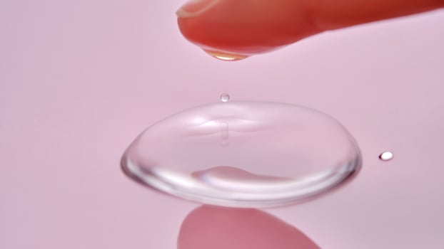 A finger touches a drop of cosmetic product on a pink background. photo