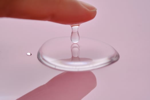 A finger touches a drop of cosmetic product on a pink background. photo